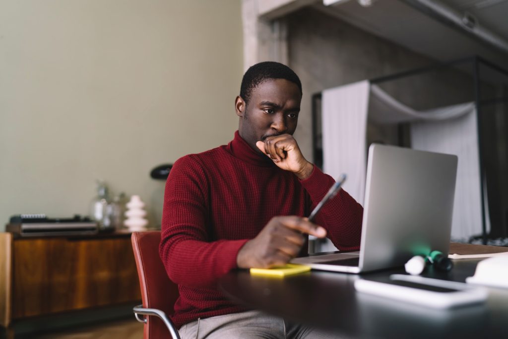 Thoughtful African American man with pen working on laptop